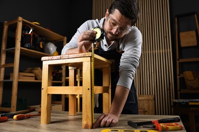 Photo of Repairman measuring wooden stool at table in workshop