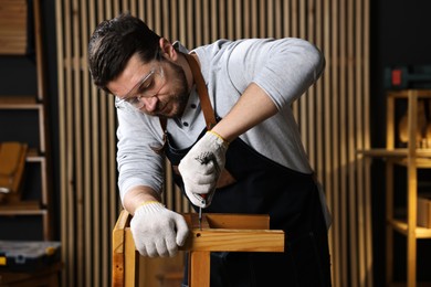 Professional carpenter repairing wooden stool in workshop