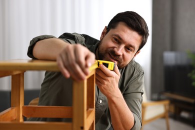 Photo of Man using tape measure while repairing wooden stool at home