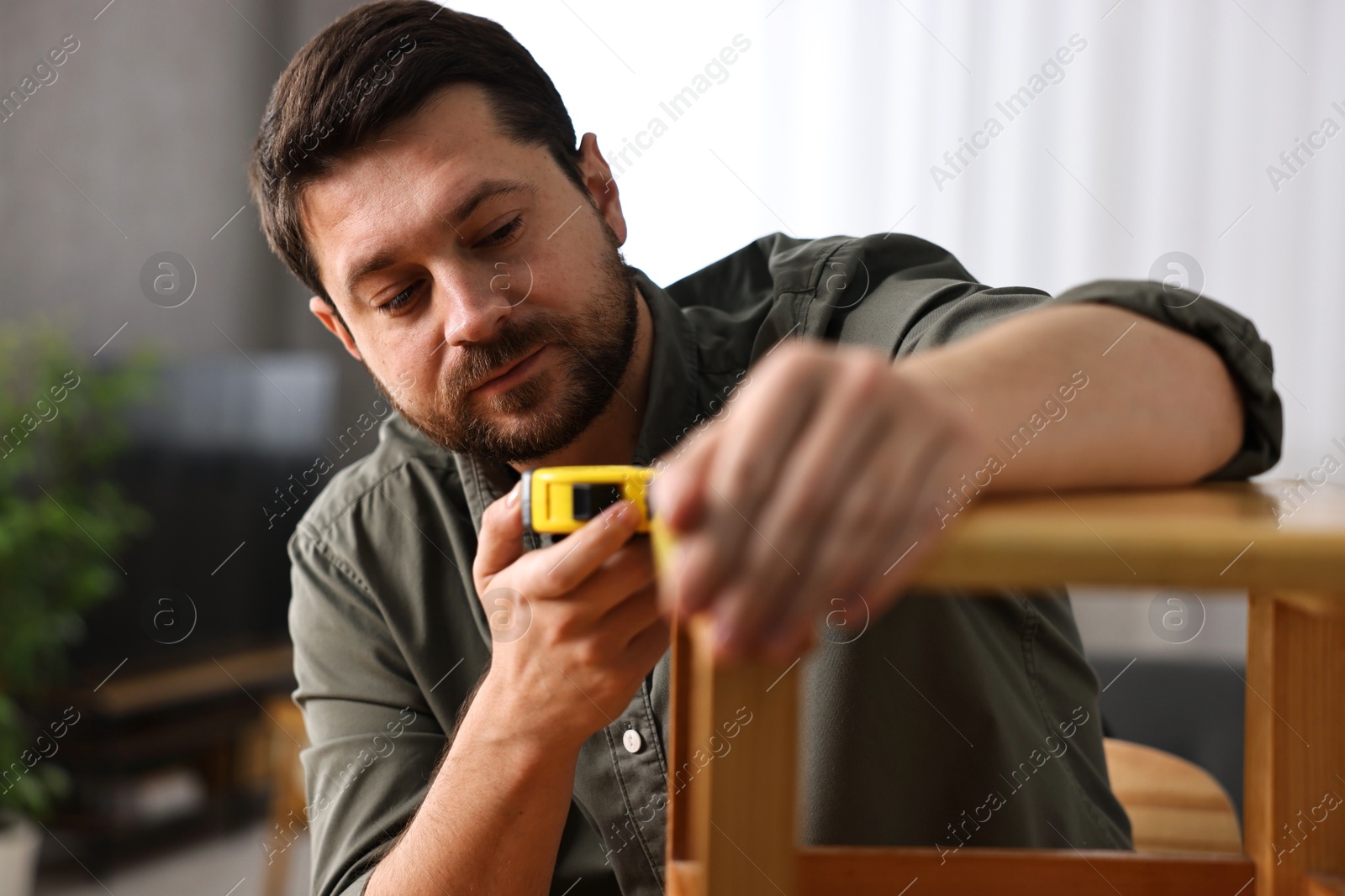 Photo of Man using tape measure while repairing wooden stool at home