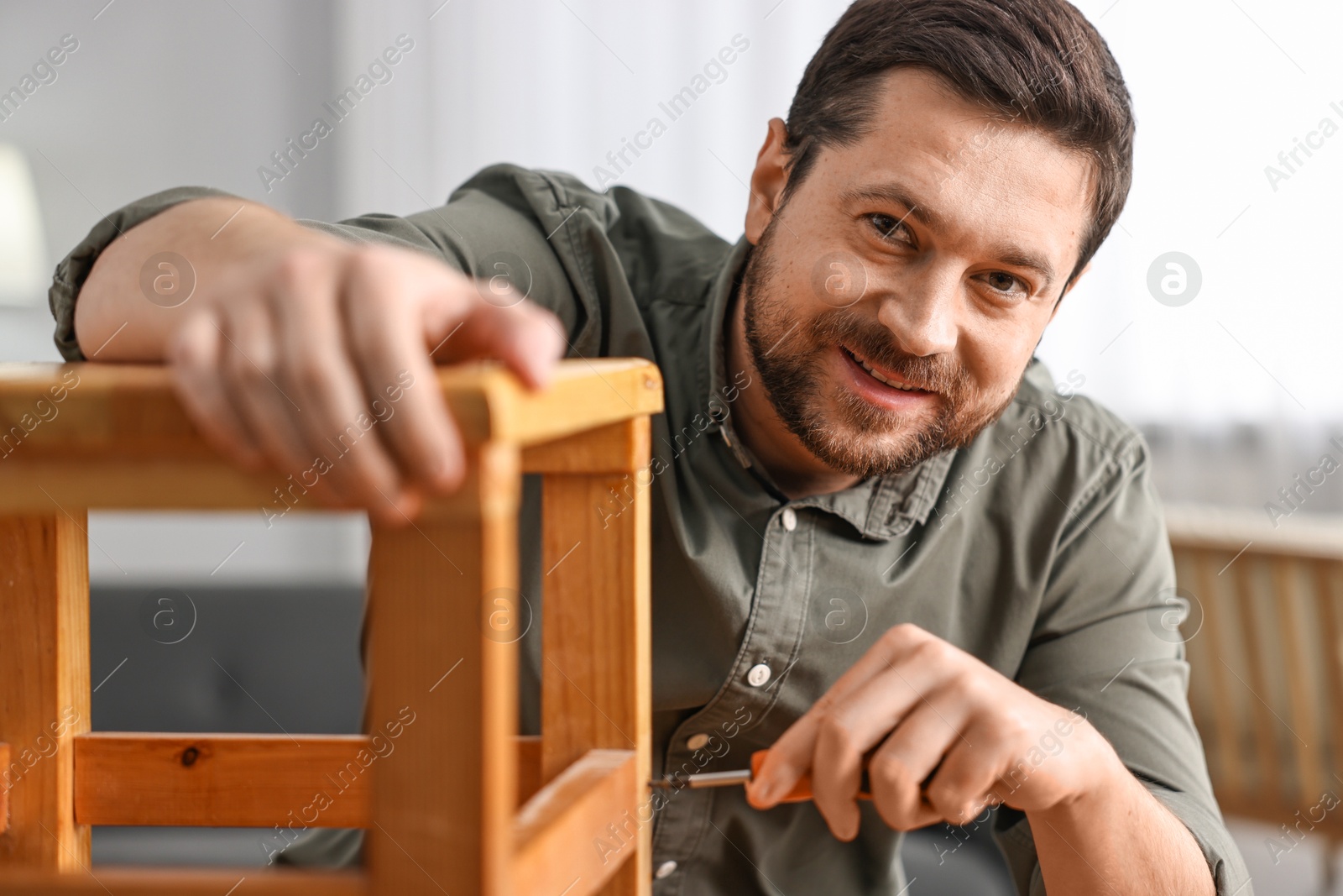 Photo of Man repairing wooden stool with screwdriver at home