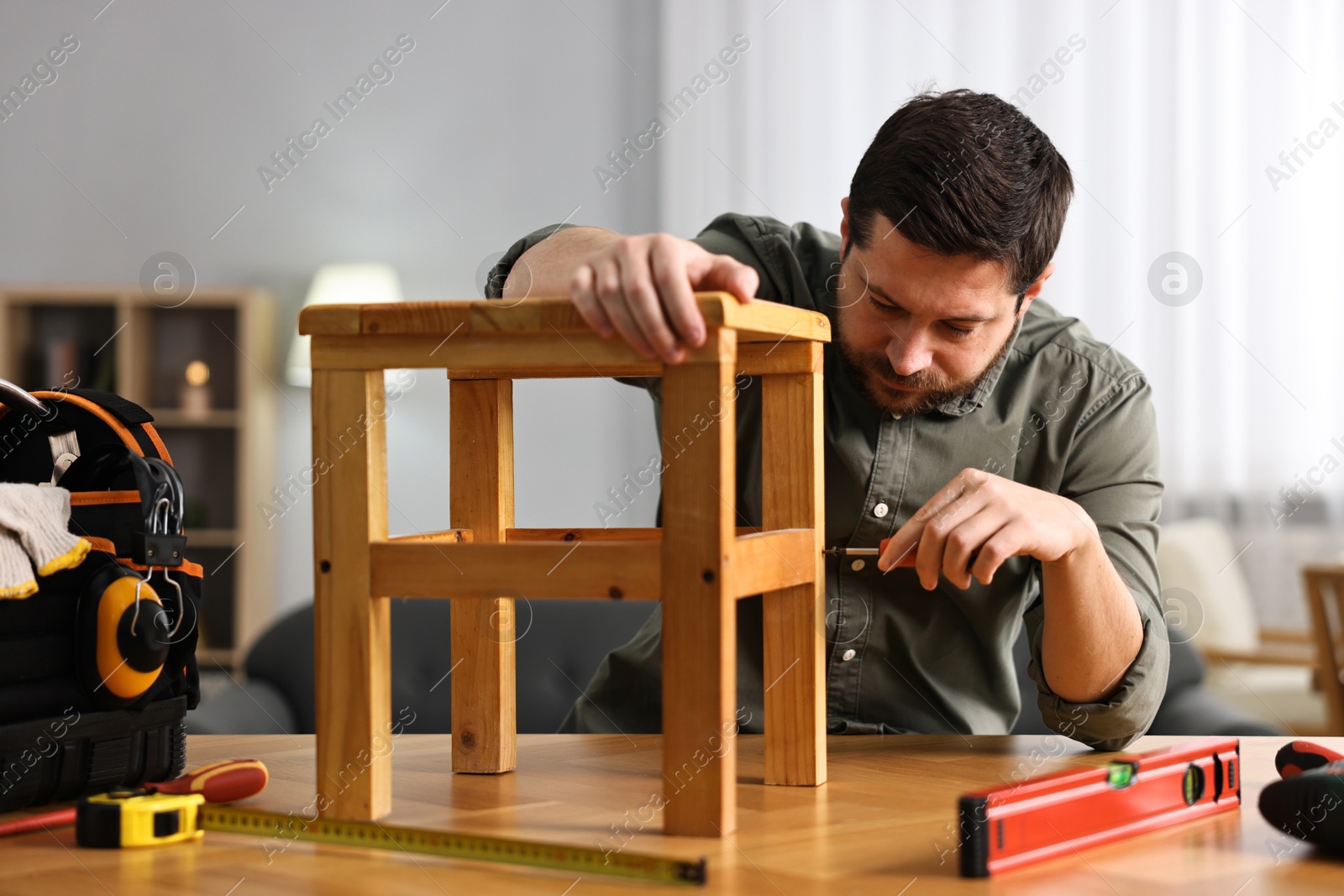 Photo of Man repairing wooden stool with screwdriver at home