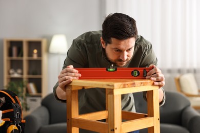 Photo of Man using level tool while repairing wooden stool at home