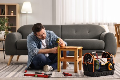 Photo of Man using tape measure while repairing wooden stool at home