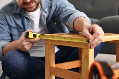 Photo of Man using tape measure while repairing wooden stool at home, closeup