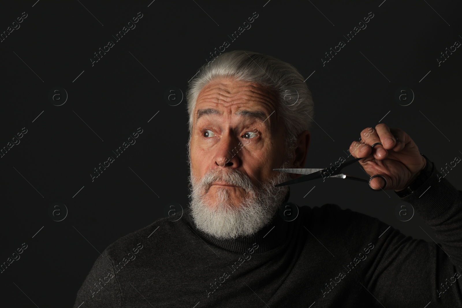 Photo of Senior man trimming beard with scissors on dark grey background