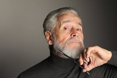 Photo of Senior man trimming beard with scissors on grey background