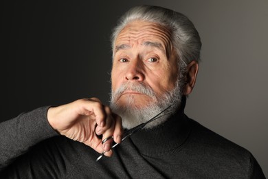 Photo of Senior man trimming beard with scissors on grey background