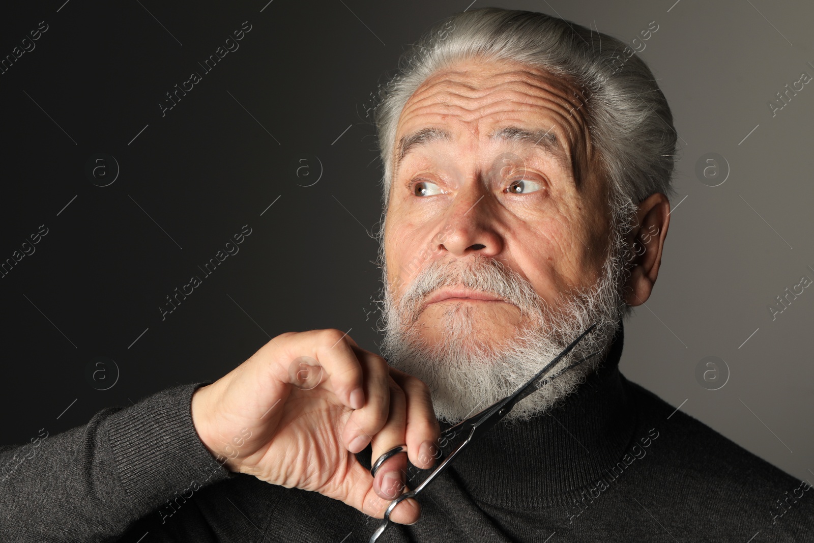 Photo of Senior man trimming beard with scissors on grey background