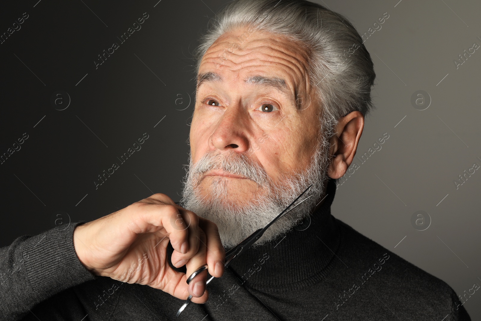 Photo of Senior man trimming beard with scissors on grey background