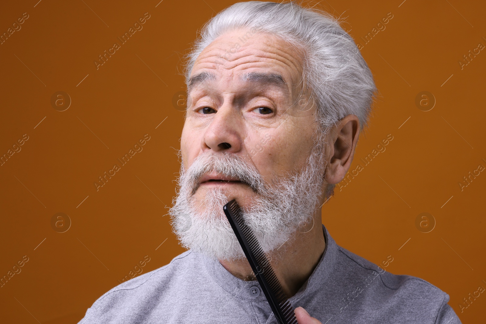 Photo of Senior man combing beard on orange background