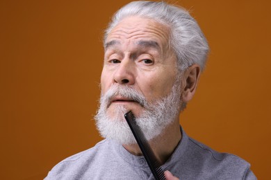 Photo of Senior man combing beard on orange background