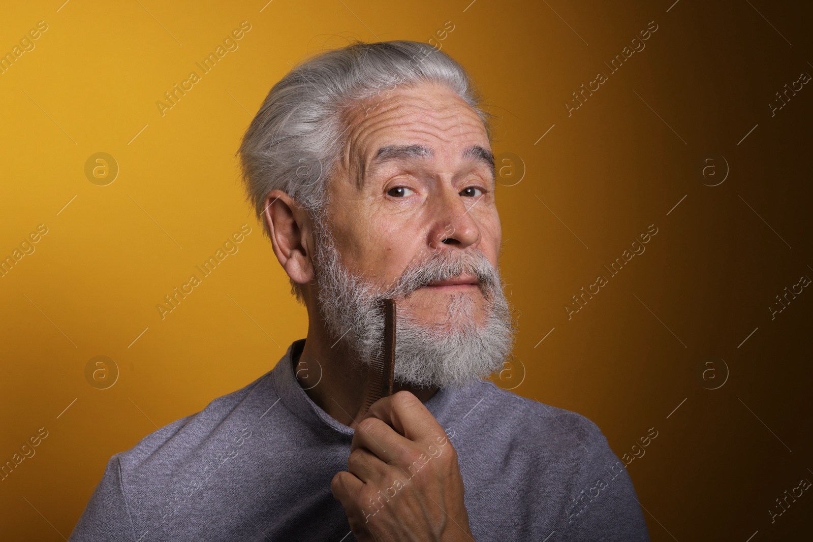 Photo of Senior man combing beard on orange background