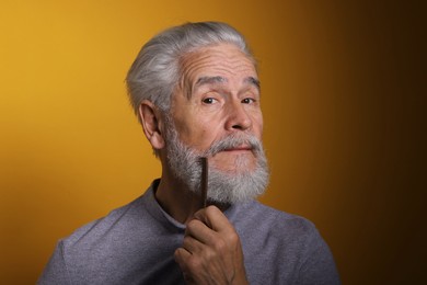 Photo of Senior man combing beard on orange background