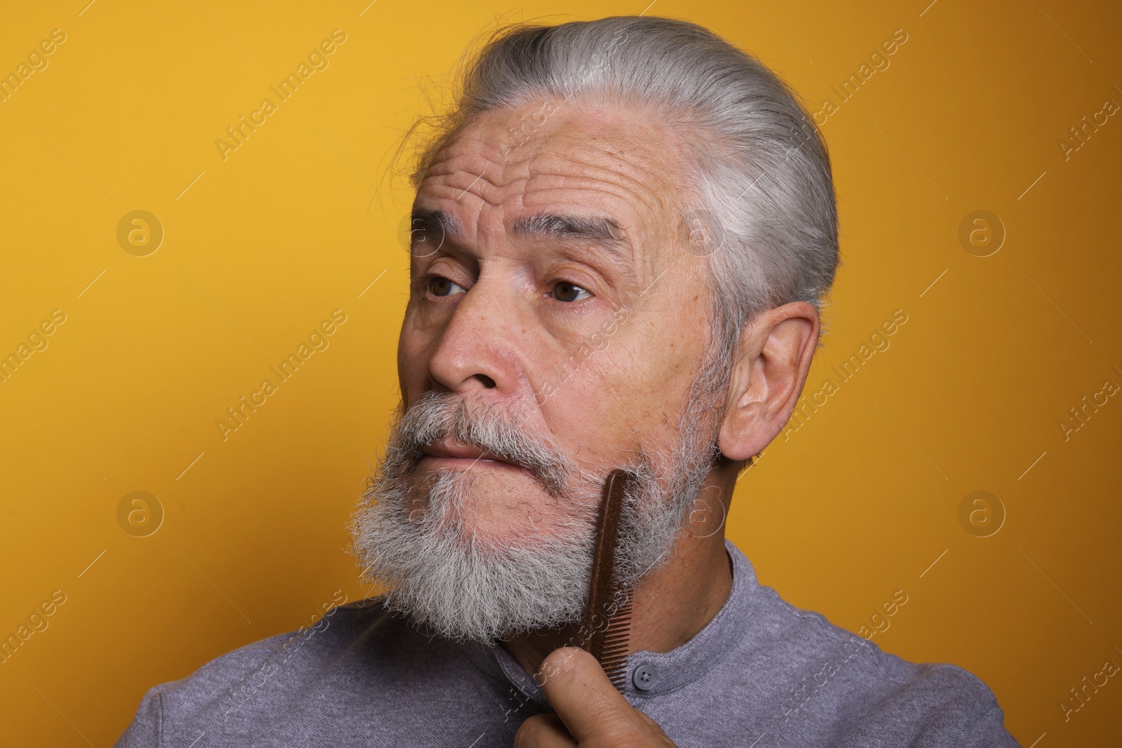 Photo of Senior man combing beard on orange background