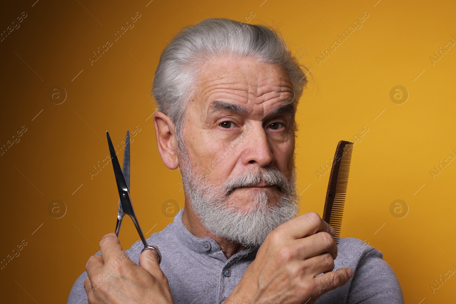 Photo of Bearded senior man holding comb and scissors on orange background