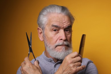 Photo of Bearded senior man holding comb and scissors on orange background