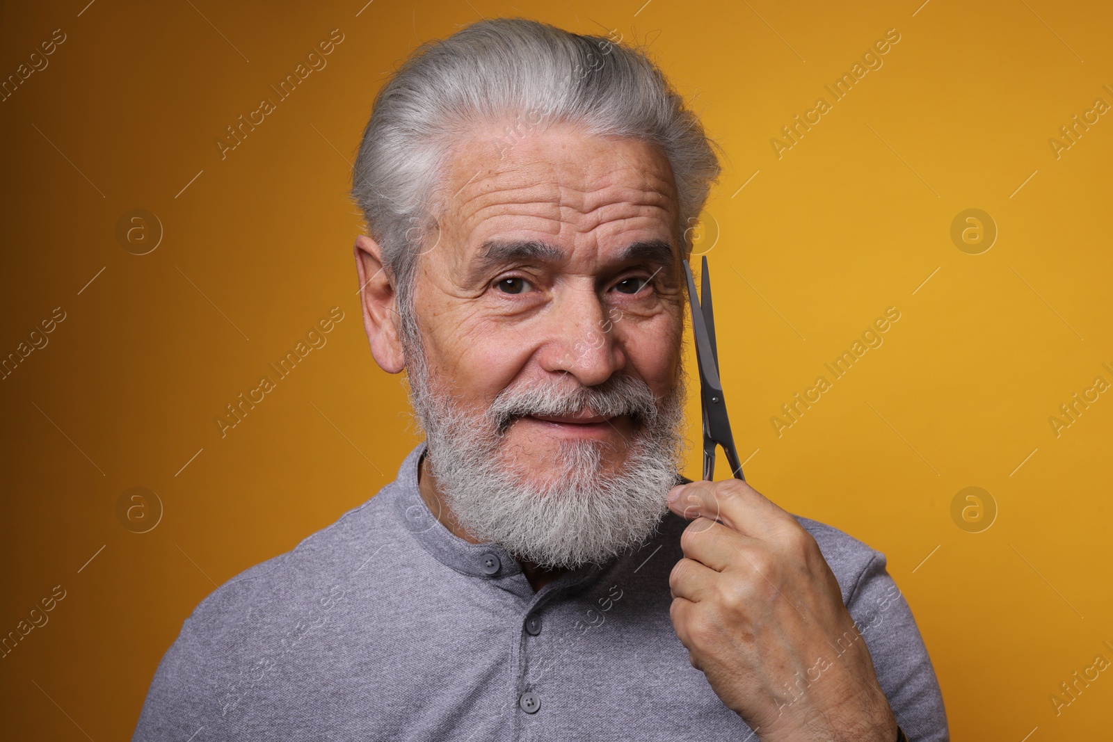 Photo of Bearded senior man holding scissors on orange background