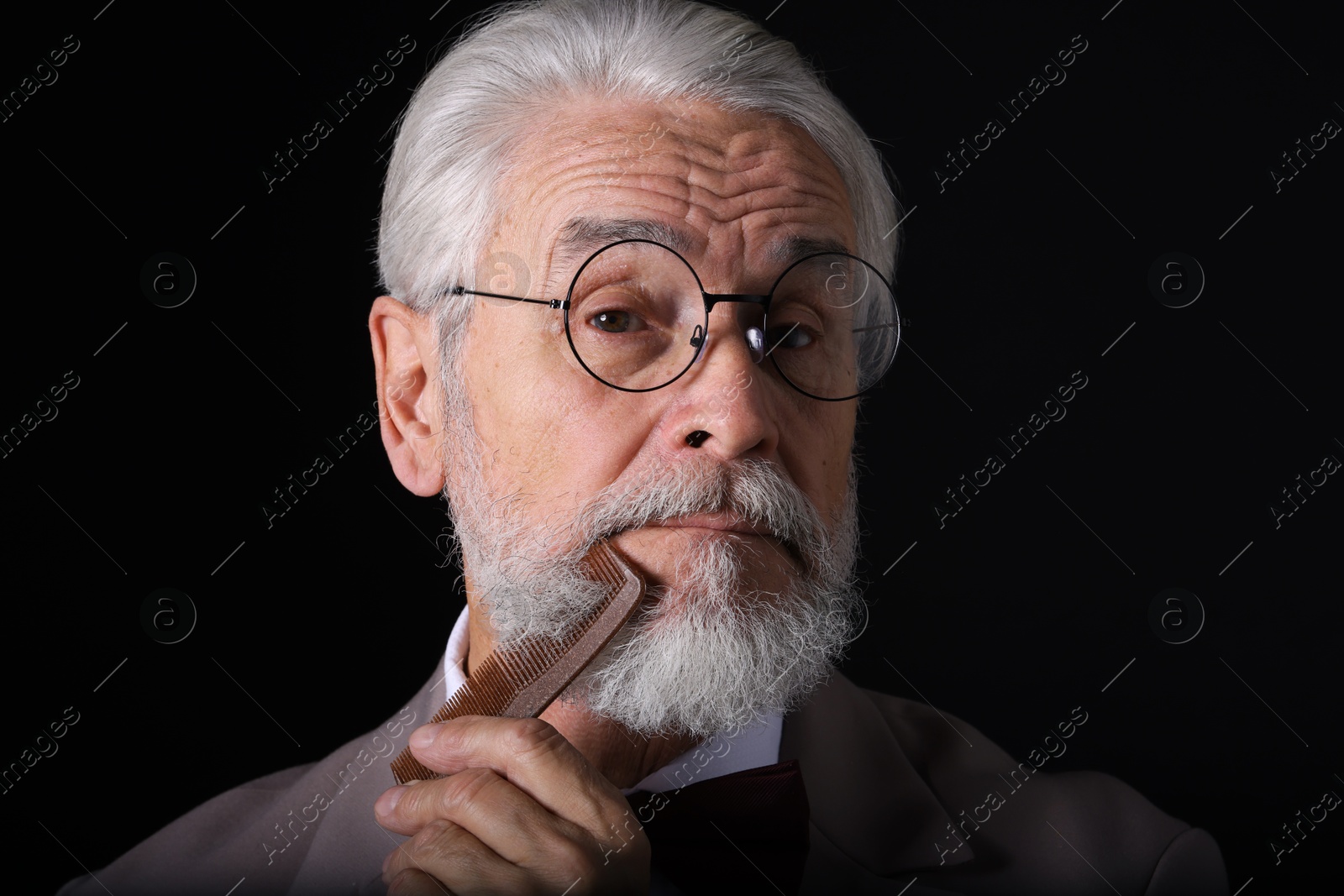 Photo of Senior man combing beard on black background