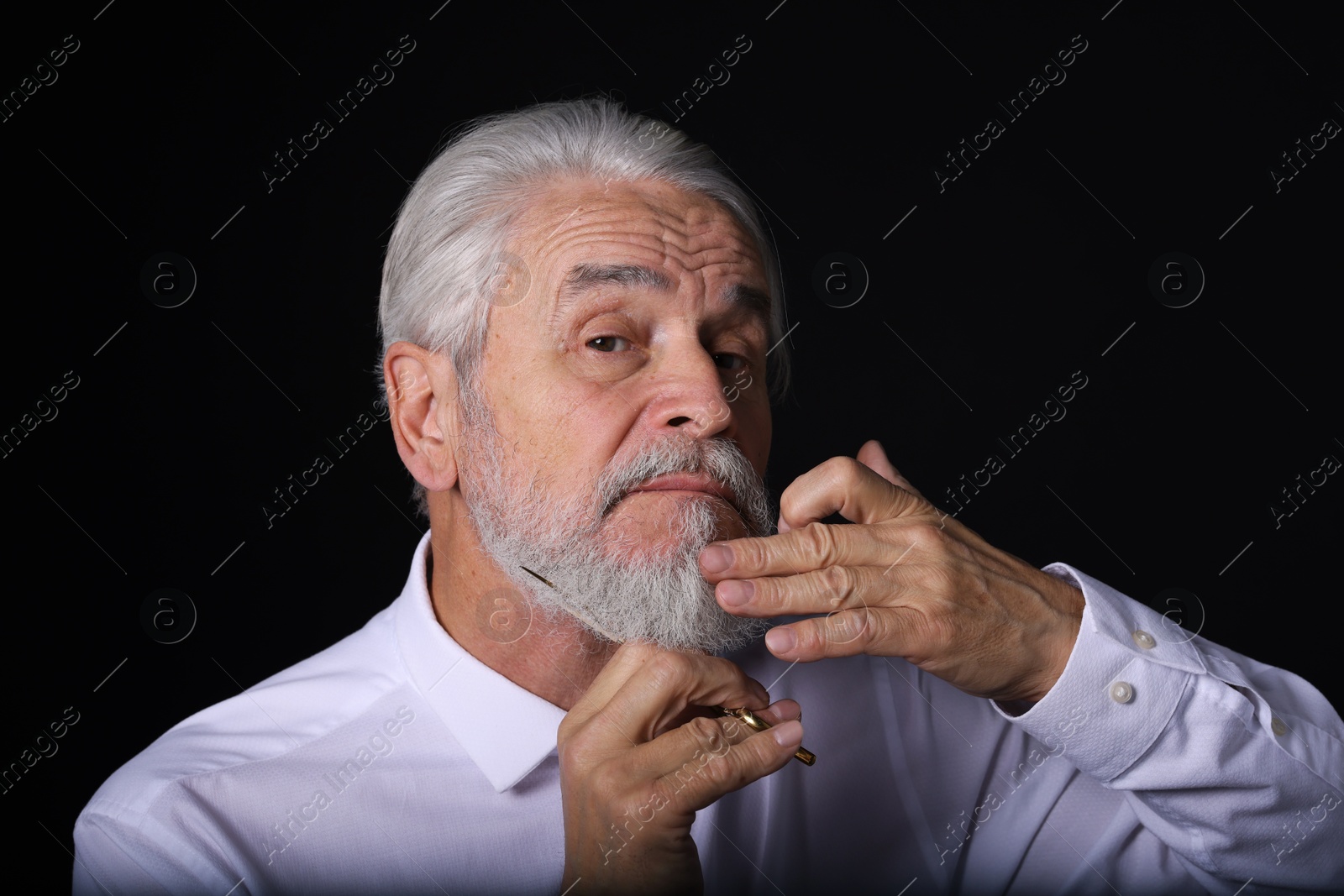 Photo of Senior man trimming beard with scissors on black background