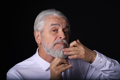 Photo of Senior man trimming beard with scissors on black background