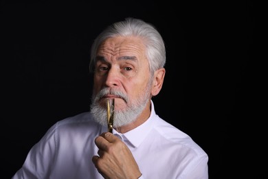 Photo of Senior man trimming beard with scissors on black background