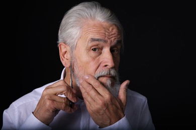 Photo of Senior man trimming beard with scissors on black background