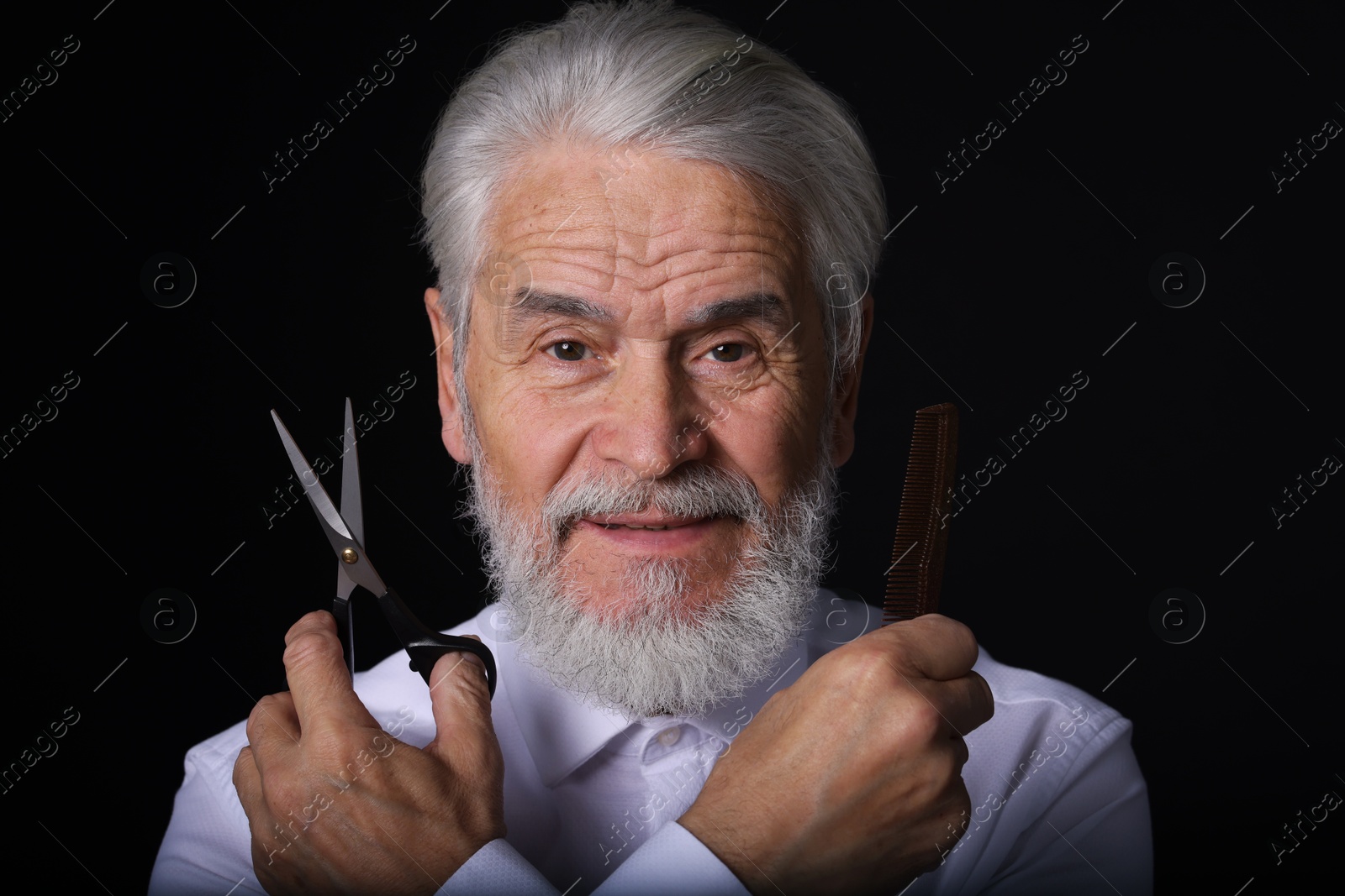 Photo of Bearded senior man holding comb and scissors on black background