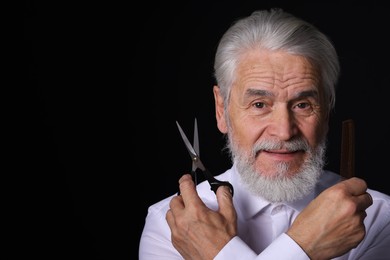 Photo of Bearded senior man holding comb and scissors on black background, space for text