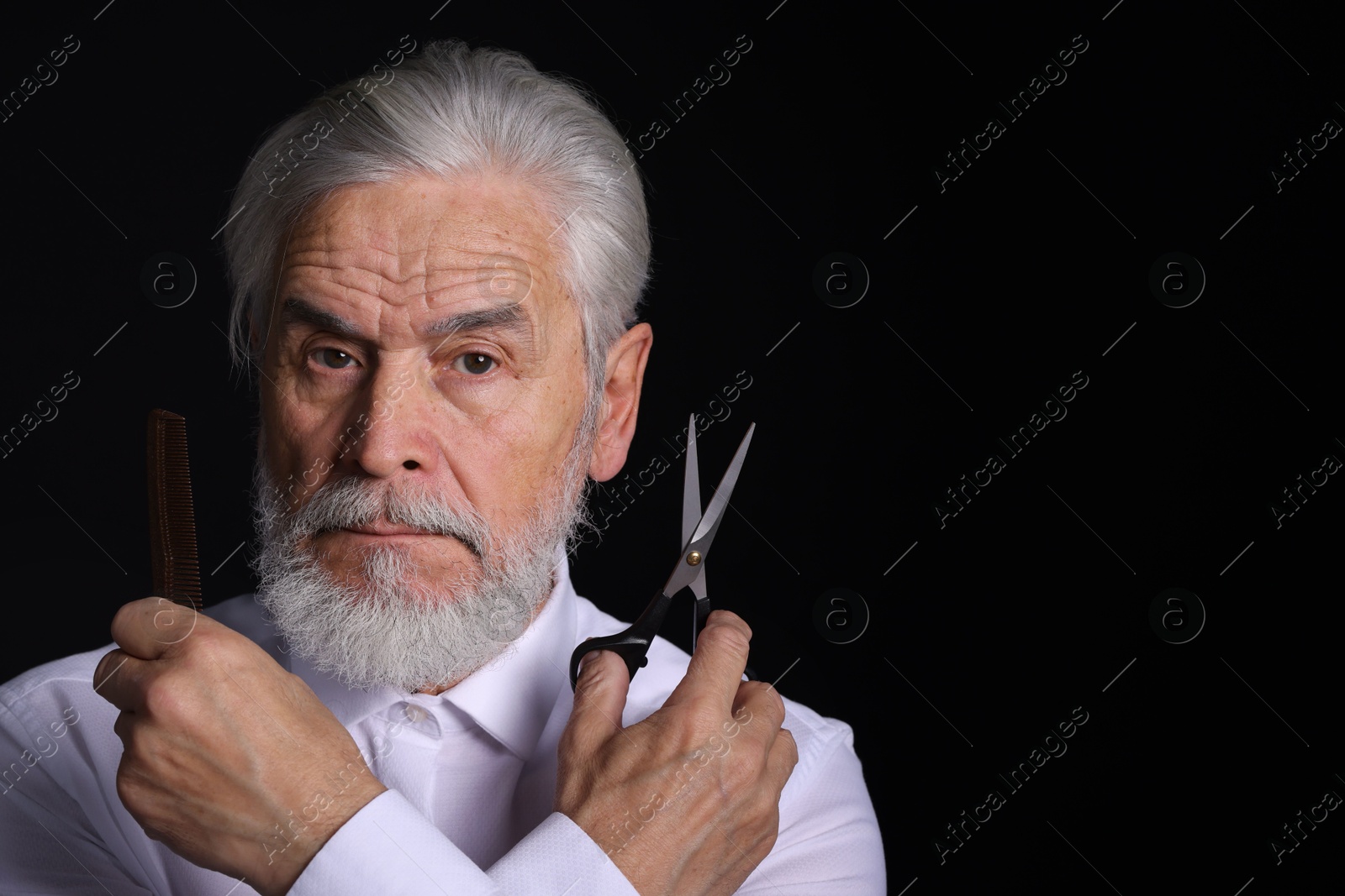 Photo of Bearded senior man holding comb and scissors on black background, space for text