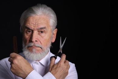 Photo of Bearded senior man holding comb and scissors on black background, space for text