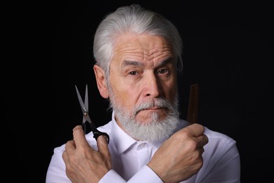 Photo of Bearded senior man holding comb and scissors on black background