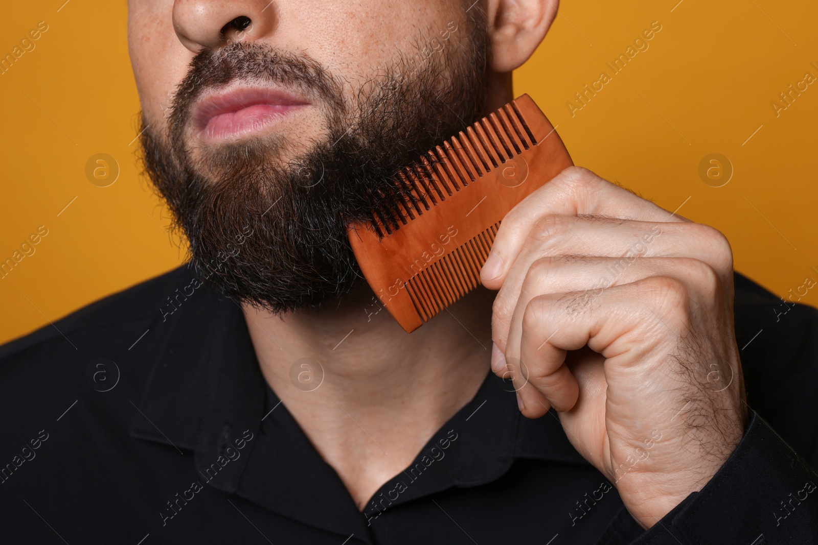 Photo of Man combing beard on orange background, closeup