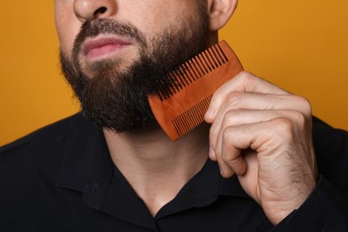 Photo of Man combing beard on orange background, closeup