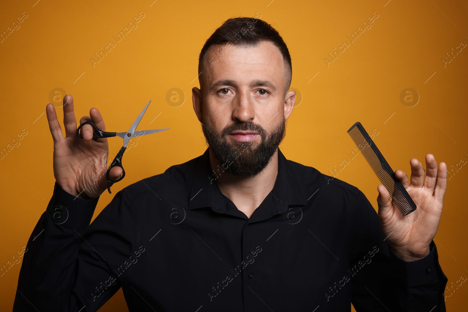 Photo of Bearded man holding comb and scissors on orange background