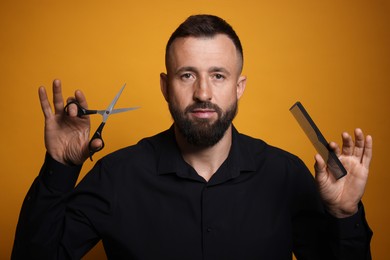 Photo of Bearded man holding comb and scissors on orange background