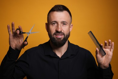 Photo of Bearded man holding comb and scissors on orange background