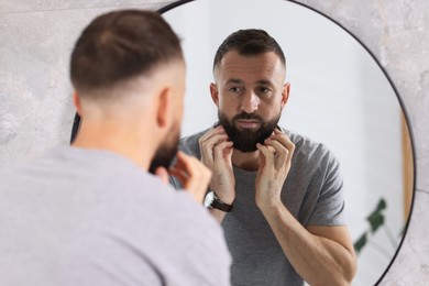 Photo of Handsome bearded man near mirror in bathroom