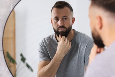 Photo of Handsome bearded man near mirror in bathroom