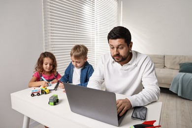 Photo of Naughty children and their overwhelmed father at table with laptop indoors