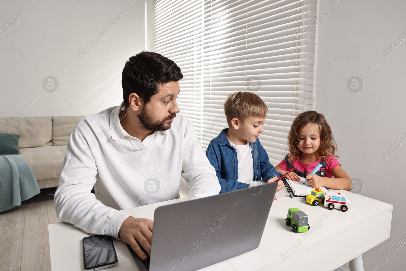 Photo of Naughty children and their overwhelmed father at table with laptop indoors