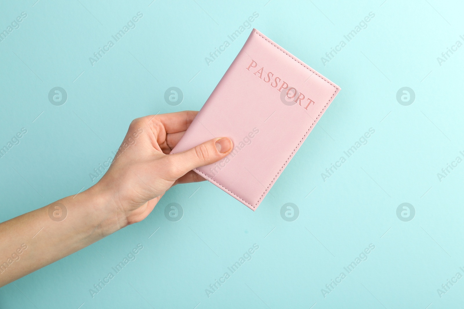 Photo of Woman holding passport in pink cover on turquoise background, closeup