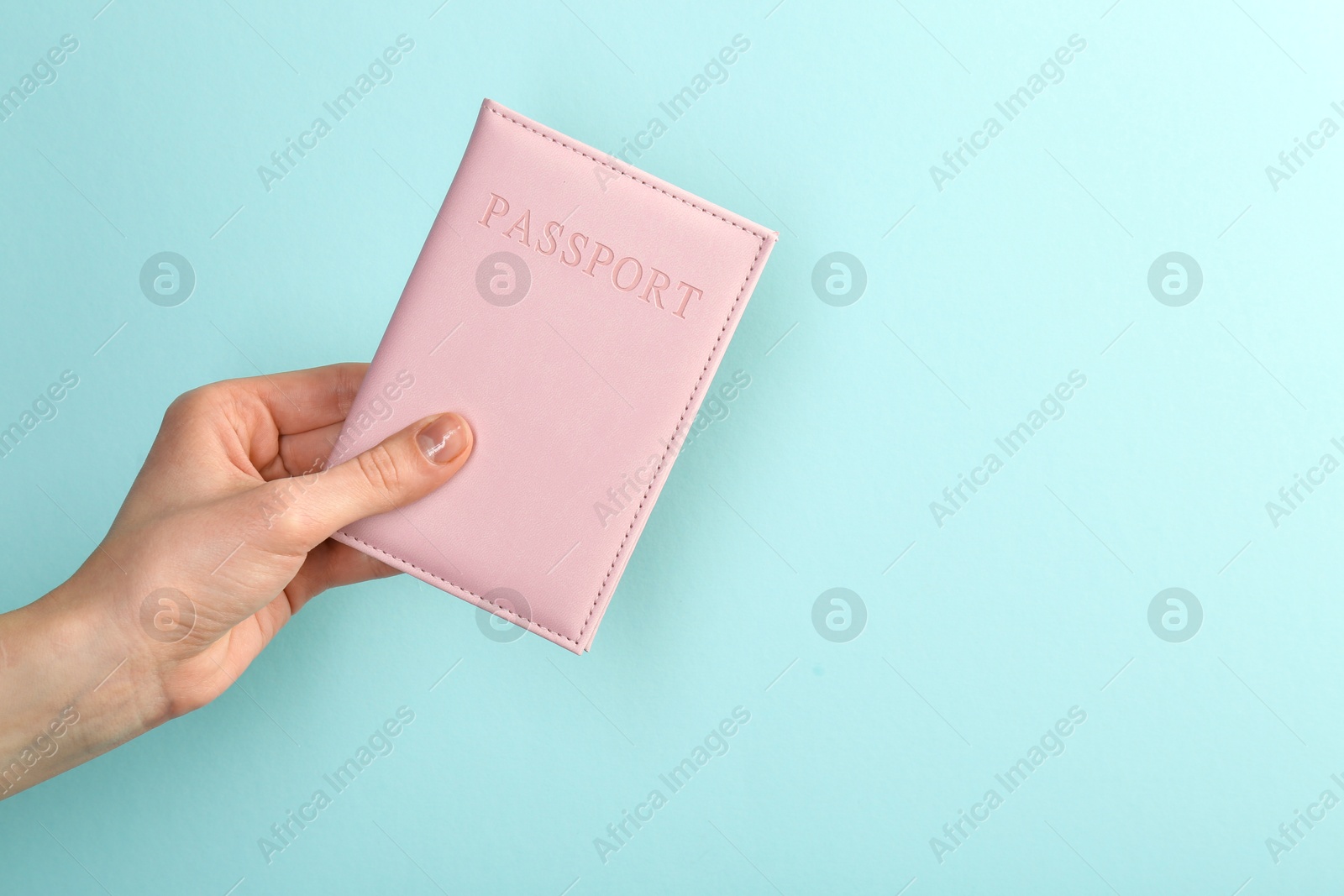 Photo of Woman holding passport in pink cover on turquoise background, closeup. Space for text