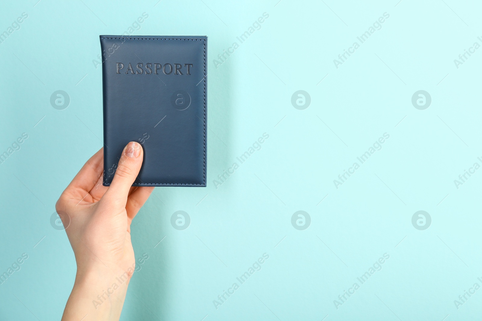 Photo of Woman holding passport in dark blue cover on turquoise background, closeup. Space for text