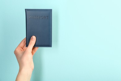 Photo of Woman holding passport in dark blue cover on turquoise background, closeup. Space for text