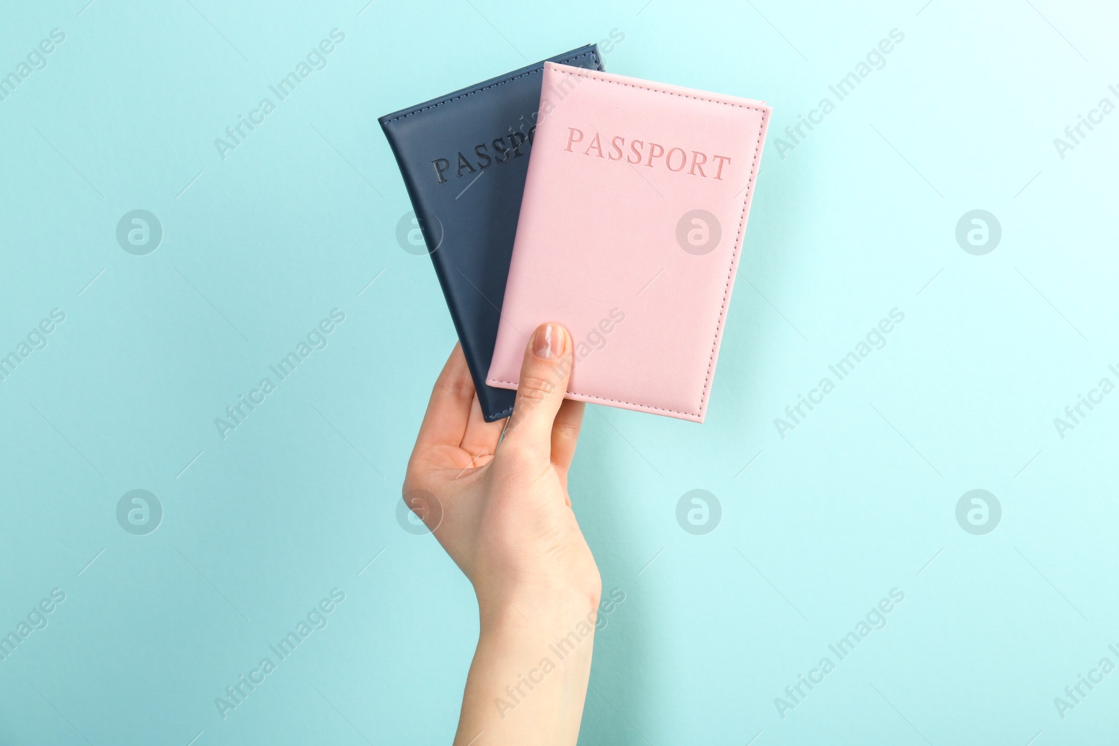 Photo of Woman holding passports in color covers on turquoise background, closeup