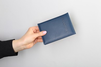 Photo of Woman holding passport in dark blue cover on light grey background, closeup