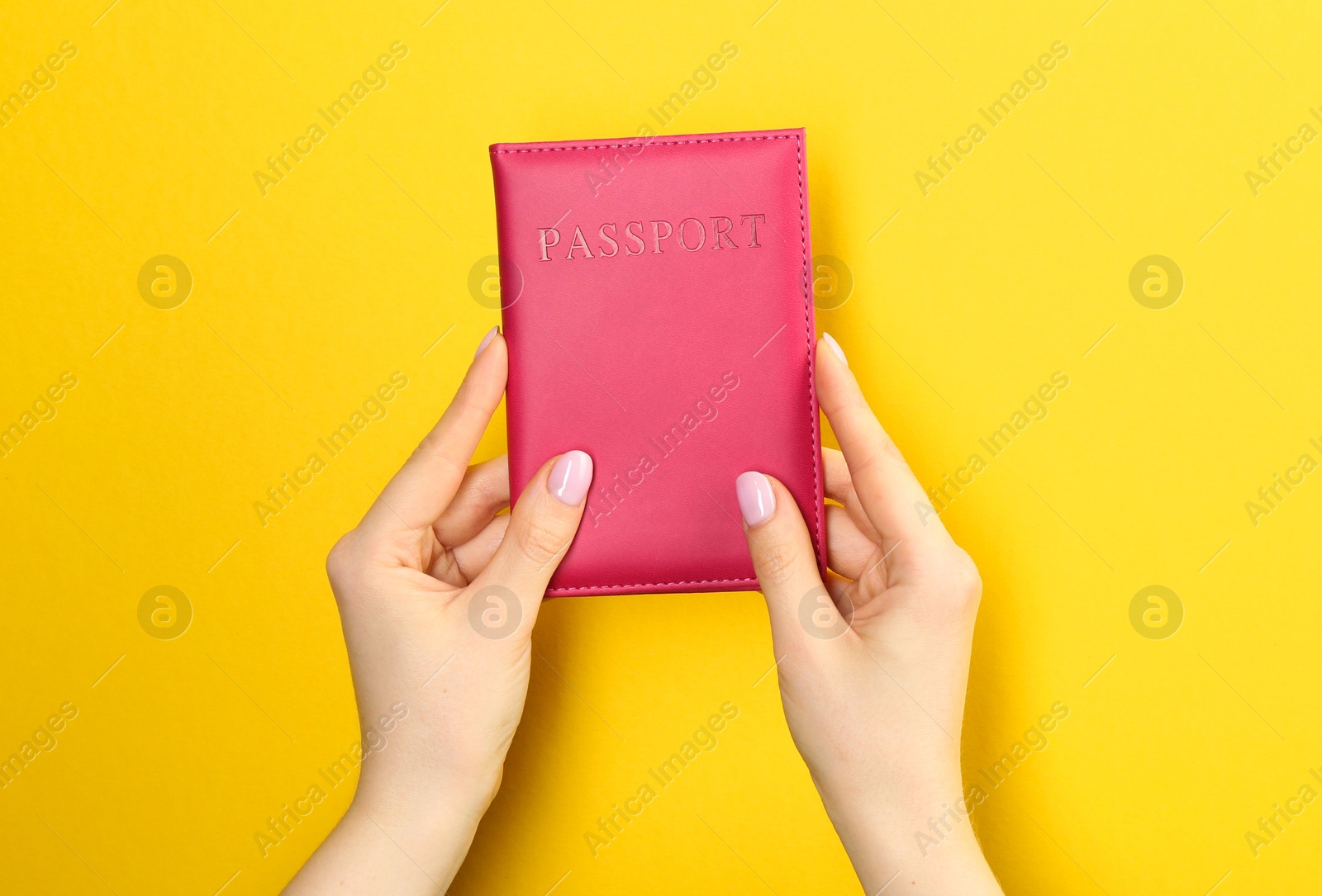 Photo of Woman holding passport in pink cover on yellow background, closeup