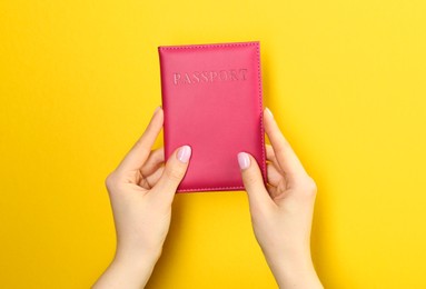 Photo of Woman holding passport in pink cover on yellow background, closeup