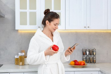 Photo of Beautiful woman with apple using smartphone after spa procedure in kitchen